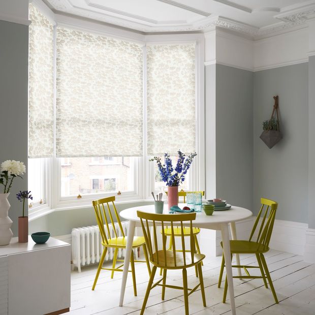 a neutral blue dining room with white and muted yellow, floral, bay window blinds and striking yellow furniture