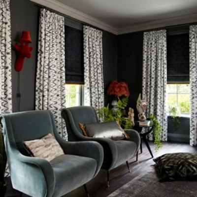 black and white curtains matched with dark coloured roman blinds in a living room with two armchairs and a sidetable