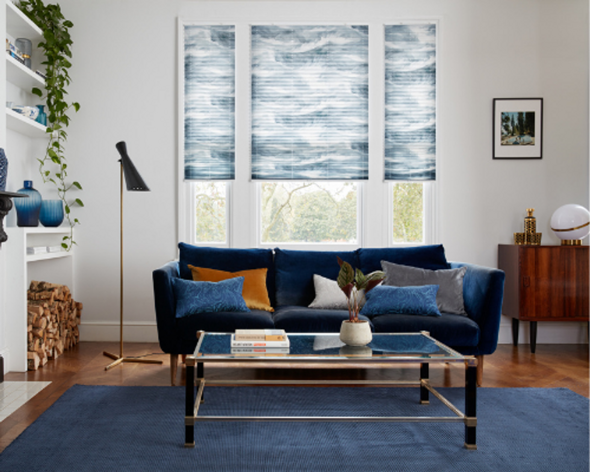 blue white and grey venetian blinds in living room with a blue rug, blue sofa, glass table and white walls and windows