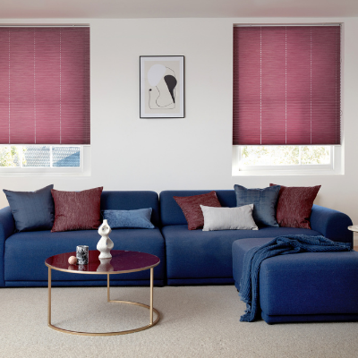 Purple coloured venetian blinds fitted to two windows in a living room with an L shaped sofa and coffee table