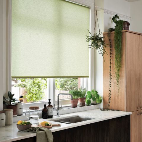 Conscious Lime roller blind made of recycled polyester displayed in a kitchen surrounded by greenery of plants and the kitchen sink