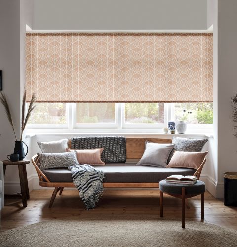 Roller blinds in a living room with a sofa facing away from the window and a small circular table next to the sofa. 