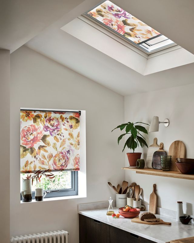 Two floral styled roller blinds, one fitted to a skylight window and another to a regular window in a white decorated kitchen