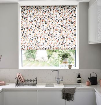 Roller blinds in a white kitchen with a sink and drying rack with some plates on it. 
