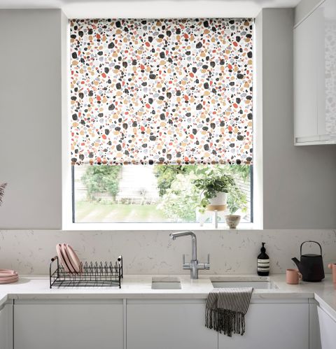Roller blinds in a white kitchen with a sink and drying rack with some plates on it. 