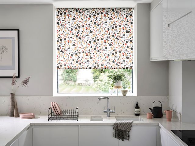 Marble kitchen with a white, blue, yellow, red and black patterned blind and warm accessories