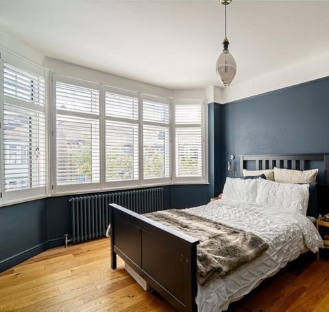 White shutters in a blue bedroom with wooden flooring and contrasting dark and light furnishings