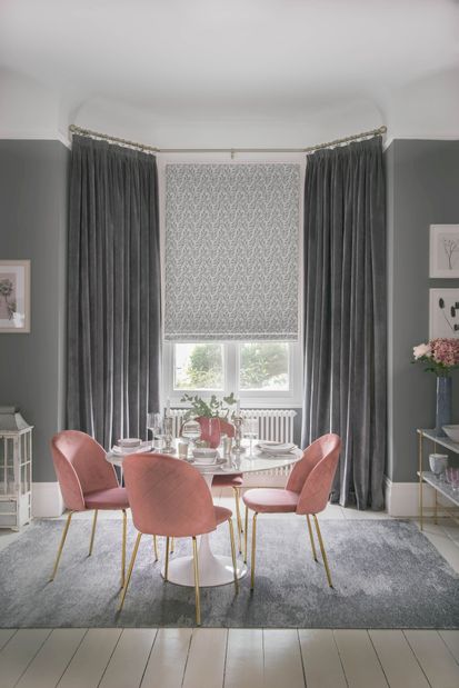 Velvet, dark grey curtains over a patterned light roman blind in a modern dining room with rose pink accents