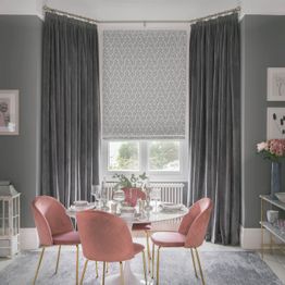 Velvet, dark grey curtains over a patterned light roman blind in a modern dining room with rose pink accents