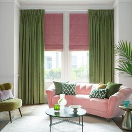 Rose pink roman blind under green curtains in a light living room with rose pink and green accents