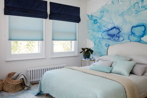 Dark blue velvet roman blind over light blue pleated blinds in a white bedroom with blue accents
