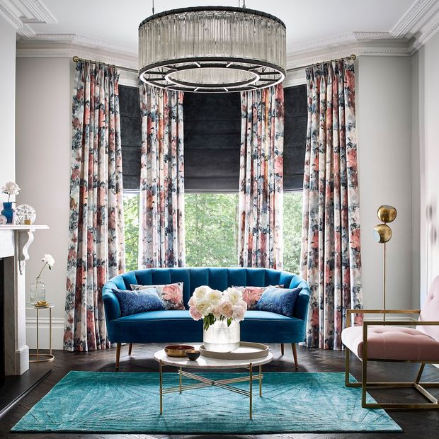 Dark grey velvet roman blind under floral print curtains in a bright living room with blue and rose pink accents