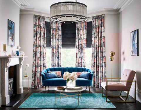 Dark grey velvet roman blind under floral print curtains in a bright living room with blue and rose pink accents