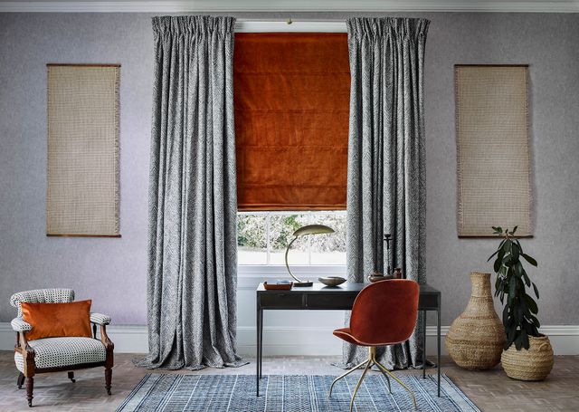 Burnt orange roman blind under grey, patterned curtains in a grey, modern study space with burnt orange accents