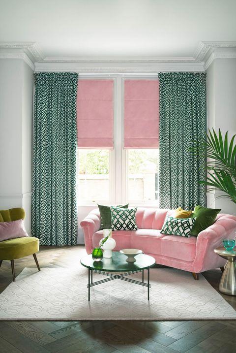 Rose pink velvet roman blind under light green patterned curtains in a modern living room with green and rose pink accents