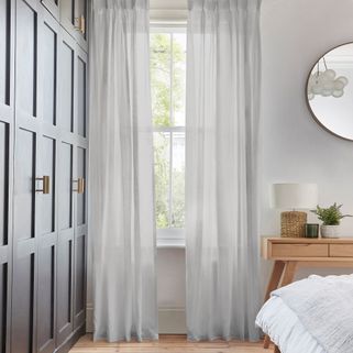 Clarity silver voile curtain displayed on an external window next to a wardrobe, slightly opened allowing light into the bedroom.