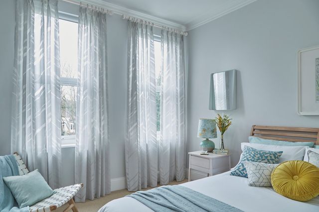 silver and white voile curtains in blue bedroom beside white table and blue bed