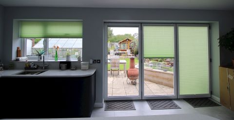 Green pleated blinds in kitchen window overlooking garden