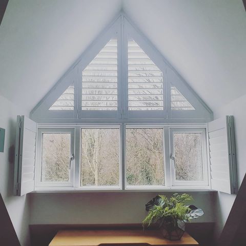 White shaped shutter in large triangle shaped bedroom window