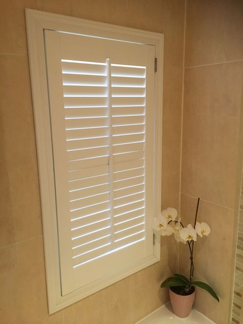 White full height bathroom shutter in small window with orchid