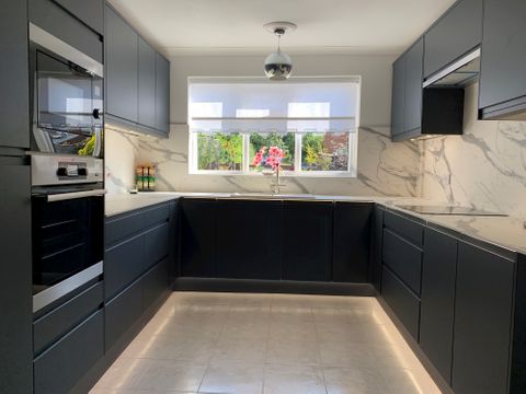 A modern, black and marble kitchen with a white roller blind