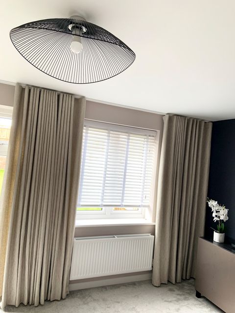 White wooden blinds under taupe wave header curtains in a bright room