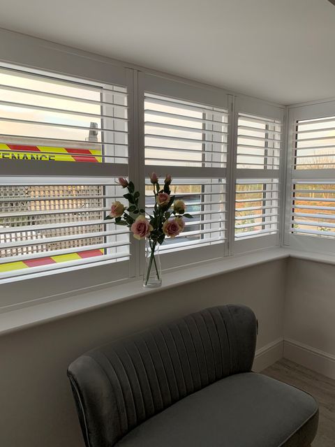 White full height shutters in box bay window with flowers on window sill