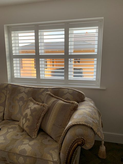 White full height shutters in small living room window with gold sofa