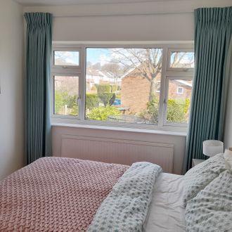 Light blue pinch pleat curtains in a bright, cosy bedroom