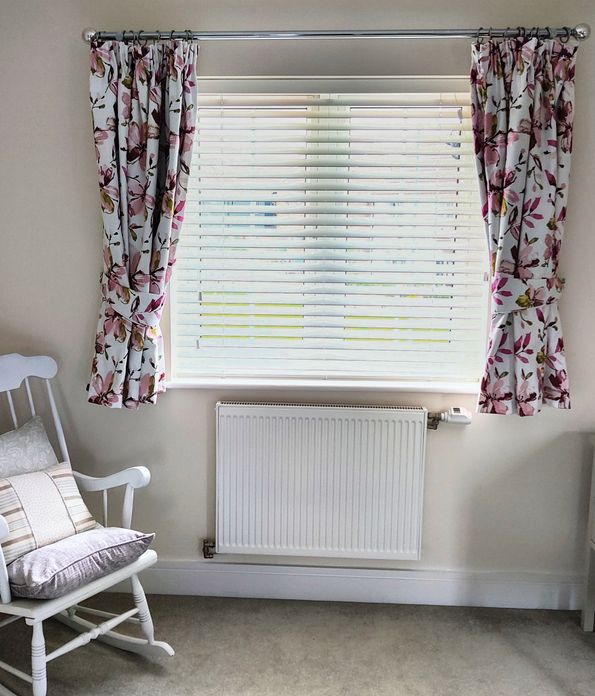 White curtains with a colourful floral print over venetian blinds in a neutral room