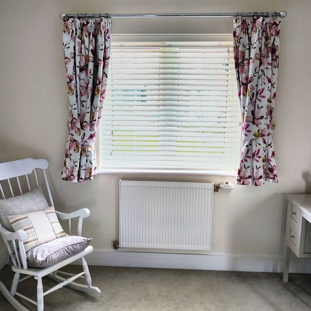 White curtains with a colourful floral print over venetian blinds in a neutral room