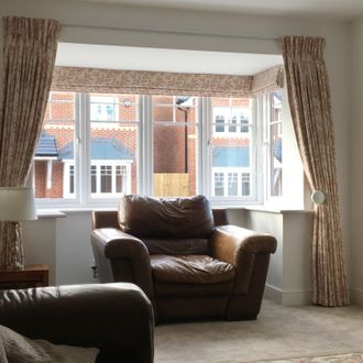 Cream pinch pleat curtains with a light brown floral print with a matching roman blind over a bay window 