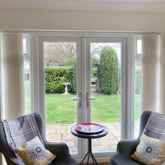 white vertical blinds fitted to a patio door in a living room with white coloured walls and two grey armchairs with a coffee table in the middle