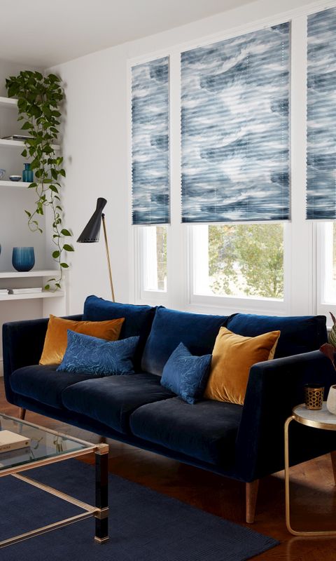 Ripple Blue pleated blind fitted to a window in a living room with white walls, sofa and glass coffee table