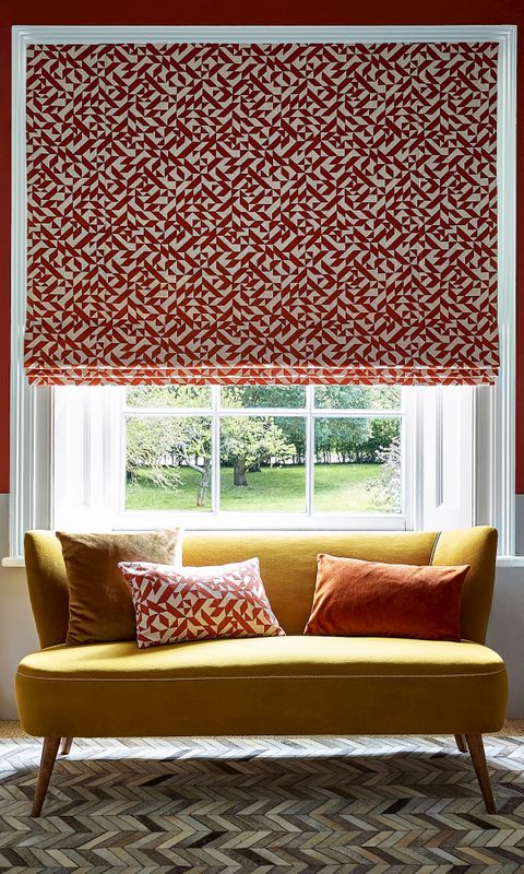 red and white roman blind with a repeating geometric pattern fitted to a window with a sofa