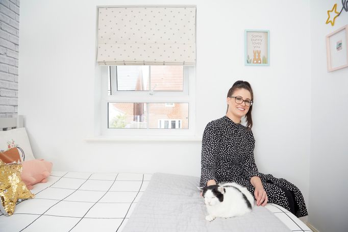 Laura Jackson sat on her bed with her cat in a bedroom with roman blinds fitted to the window