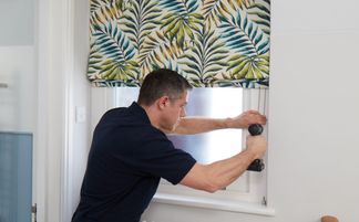 an installer fitting a roman blind to a window in a customer home