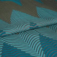 Folded Zaha Deep Teal folded fabric with a repeating leaf pattern in blue and brown colours 