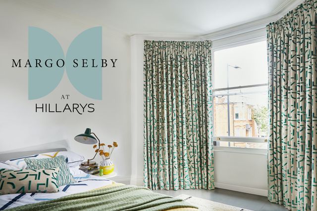 Margo Selby curtains in a bedroom, the curtains on the window on the right hand side and a white bed on the left. There is the Hillarys and Margo Selby logo on the image. 