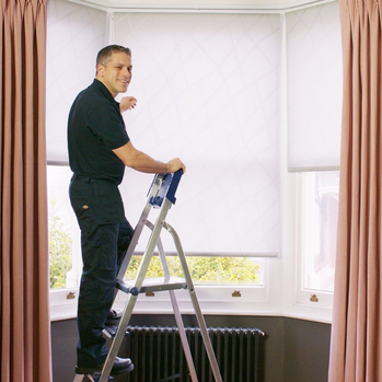 an advisor installing white roller blinds and curtains to a bay window in a customers home