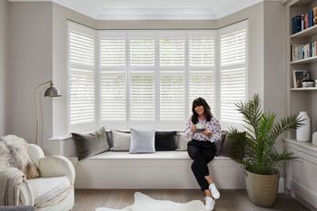 Anna Richardson sat in front of a bay window with white tier on tier shutters fitted to the window