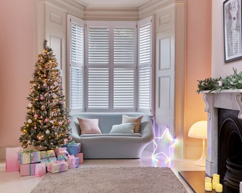 White shutters in a living room with a sofa facing away from the windows. A fireplace on the right side and a christmas tree next to the sofa. A light up star ornament is next to the sofa. 