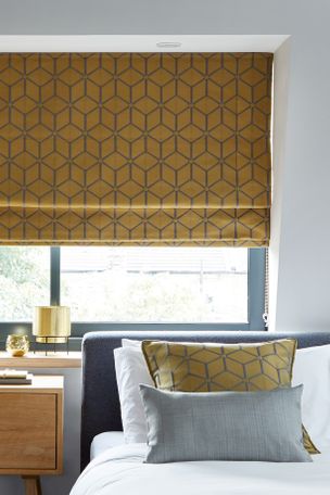 Nexus brushed gold Roman blind in window of neutral bedroom with matching Nexus brushed gold cushion