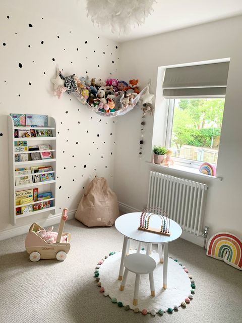 Children's bedroom with toys and a bookshelf and a small table in the middle of the room with Roman Blinds at the window 