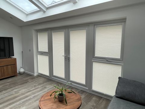 Pleated blinds in a living room with a sofa on the right side and a tv on the left side. 