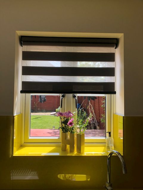 Day and Night blinds at a small window with flowers in a vase on the window sill