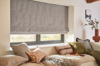 Nest Pewter Roman Blind in a bedroom with throw pillows and a fluffy blanket