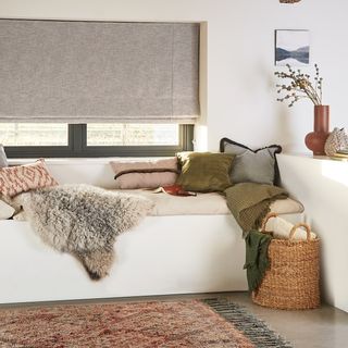 Nest Pewter roman blind in a bedroom with a blanket and throw pillows on the bed