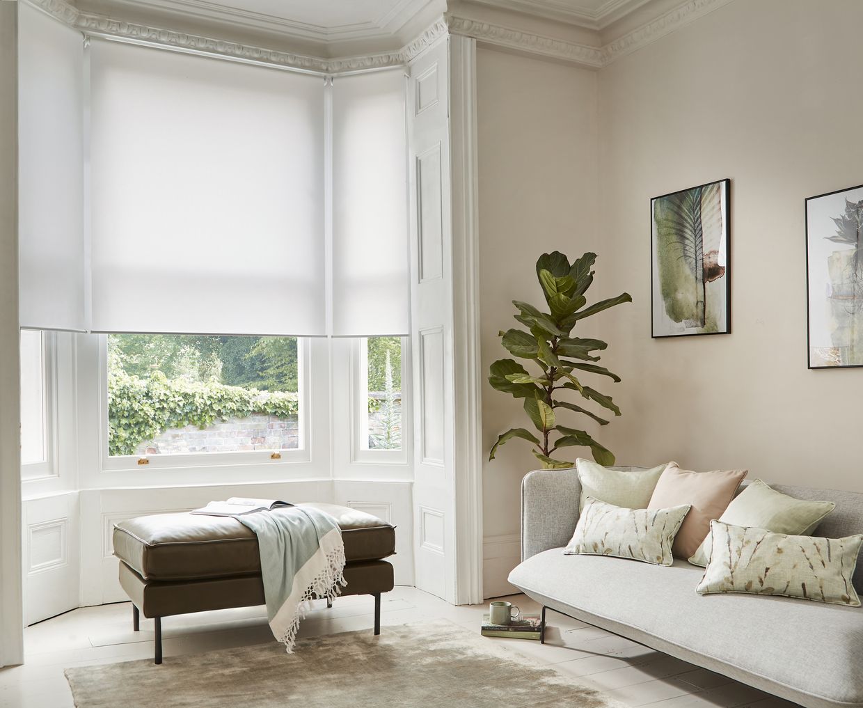 an off white, oyster coloured roller blind on a large window in a tall living room containing a brown stool and light grey sofa