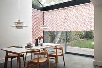 Red and white patterned roller blinds fitted to tall windows in a dining room with dining table and chairs